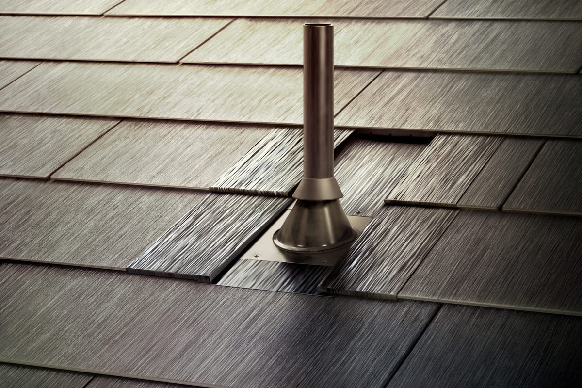 A close-up of a Tesla Solar roof near and around a small, metal chimney