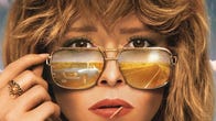 Actor Natasha Lyonne curiously peeks over the top of her retro sunglasses with a 70s muscle car reflected in the lenses.