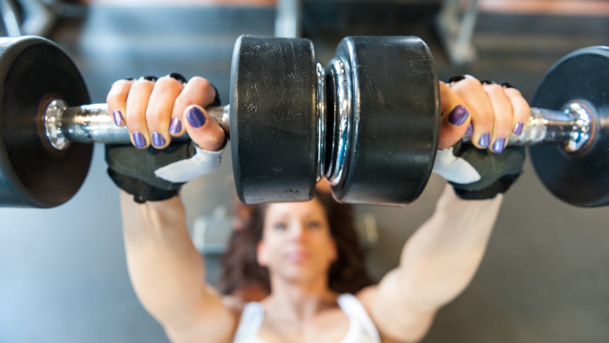 Overhead view of a woman laying on a bench and lifting dumbbells.