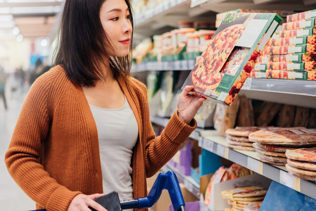Young woman looking at a frozen pizza in the grocery store.
