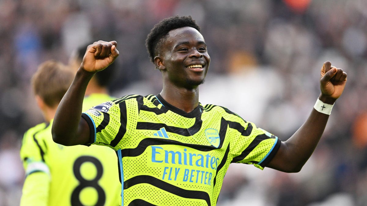 Arsenal forward Bukayo Saka celebrating, smiling with both hands clinched and raised.