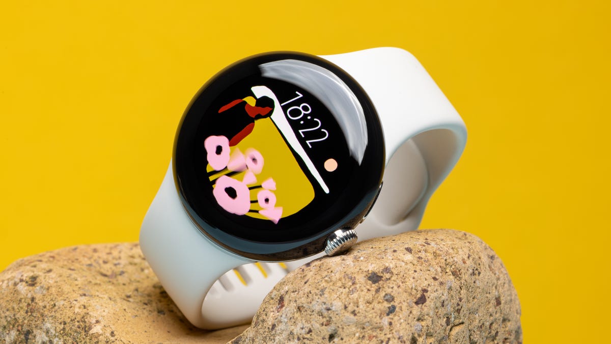 The first-generation Google Pixel Watch sitting on a rock against a yellow background
