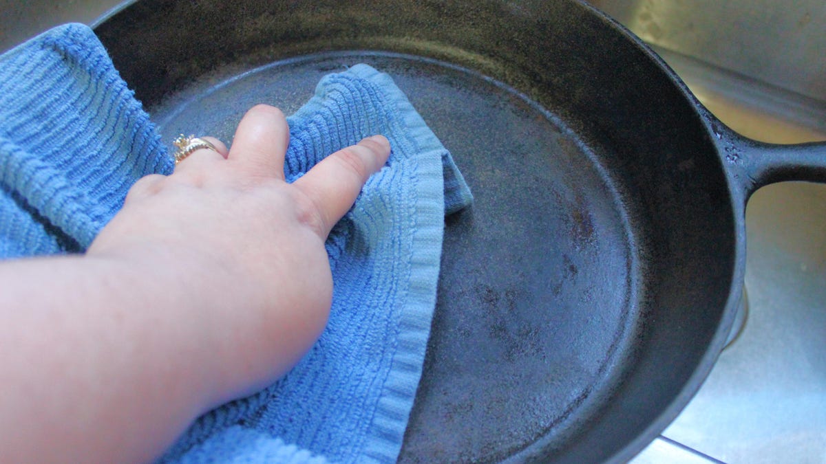 Hand wiping down a cast-iron skillet