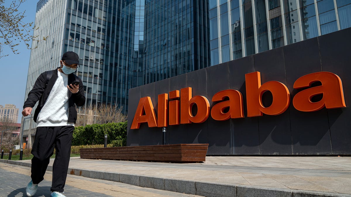 Man looking at phone walks past Alibaba sign