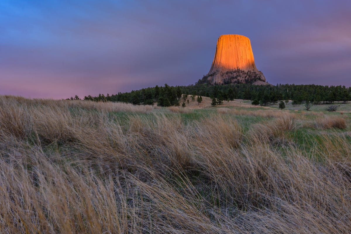 Last light breaks through the clouds and lights up the Devils Tower National Monument and surrounding clouds just before sunset in Wyoming.