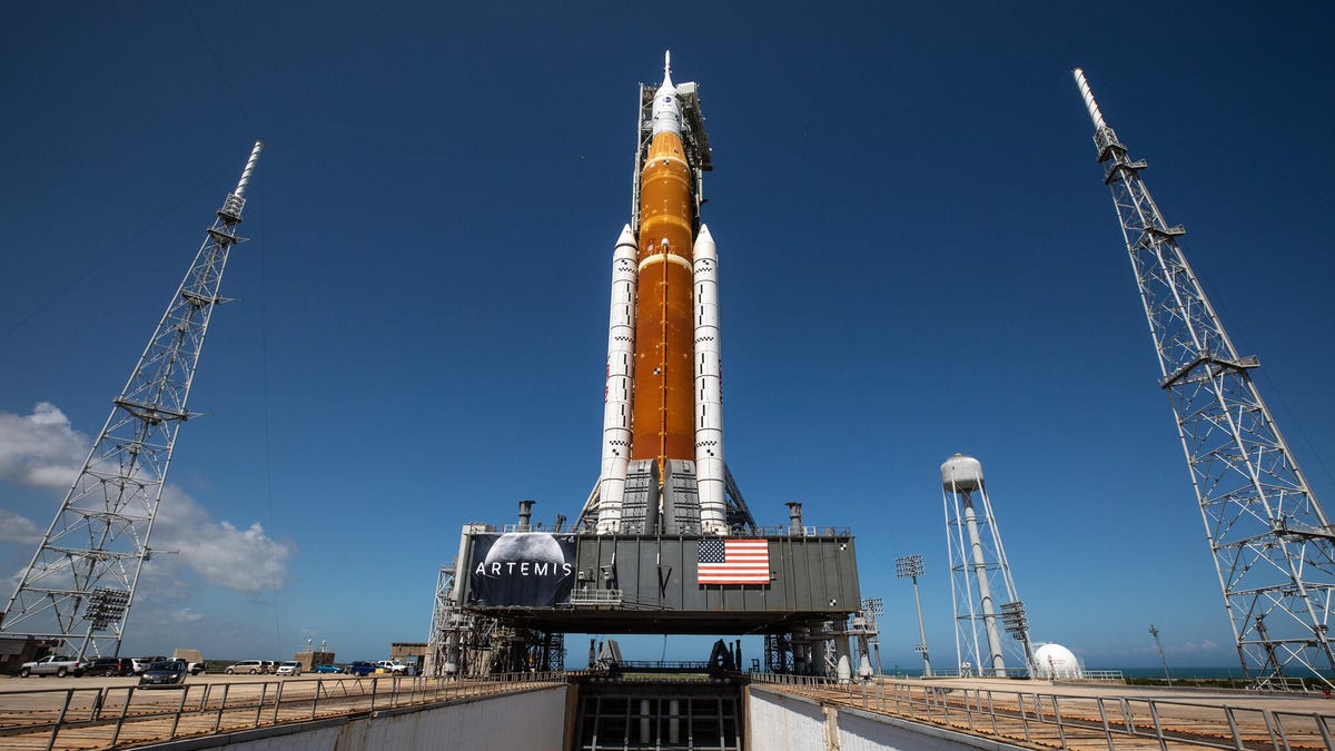 NASA's orange Artemis I rocket as seen from a low angle, a blue sky is in the background.