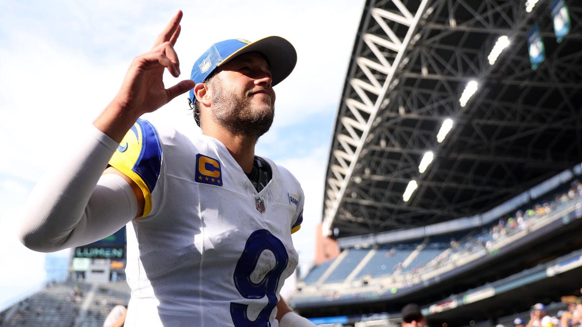 Los Angeles Rams quarterback Matthew Stafford wearing a cap and two fingers of his right hand pointing toward the sky.