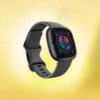 A gray Fitbit Sense 2 fitness tracker against a yellow background.