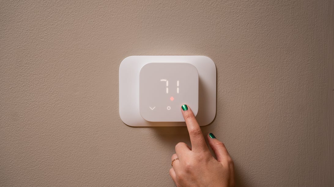 A person's hand setting a thermostat
