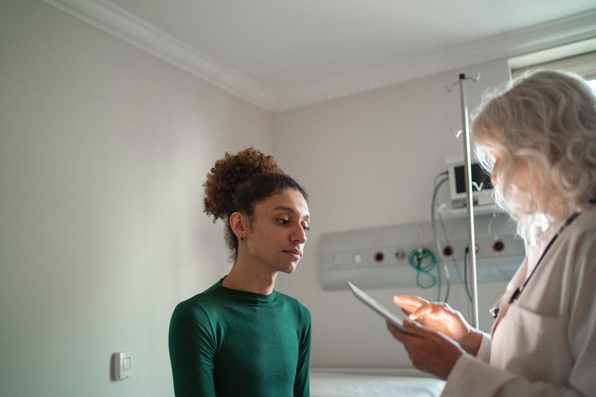 Una persona de pelo blanco con bata habla con un paciente que presenta fluidez de género.