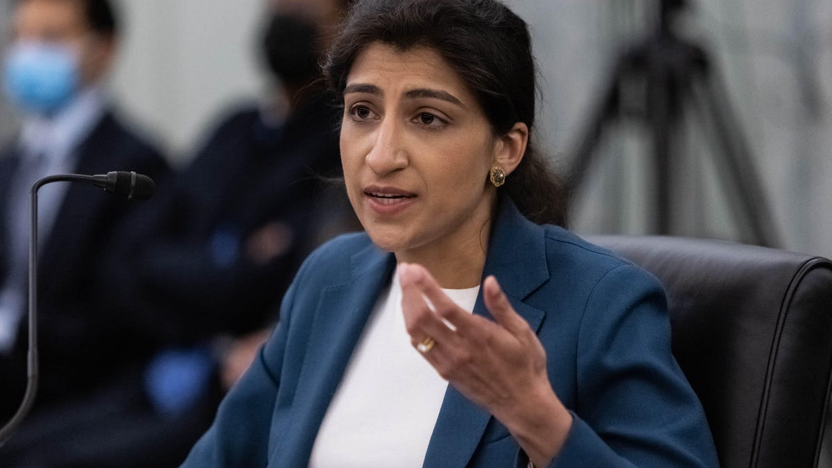 Lina Khan gestures while speaking before a small microphone at a Senate confirmation hearing.