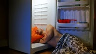 Shirtless man sleeping on the floor with his upper body inside an open fridge