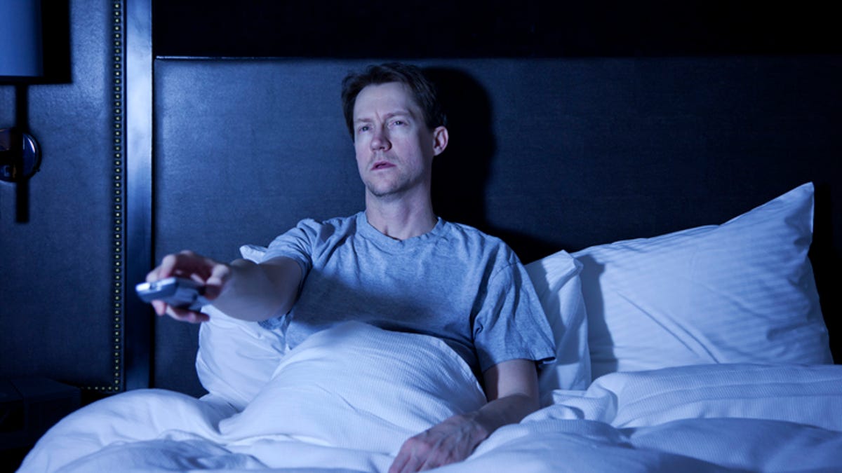 Man sitting up in bed adjusting the volume on his television.