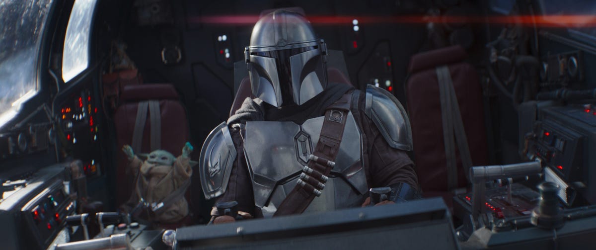 The Mandalorian pilots a spacecraft, with Baby Yoda sitting nearby.