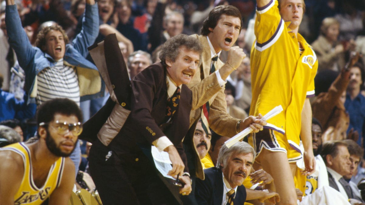 Los Angeles Lakers player Kareem Abdul-Jabbar (seated left, wearing goggles) and coach Jerry West (standing center, beige suit) celebrate at the Forum in 1977.