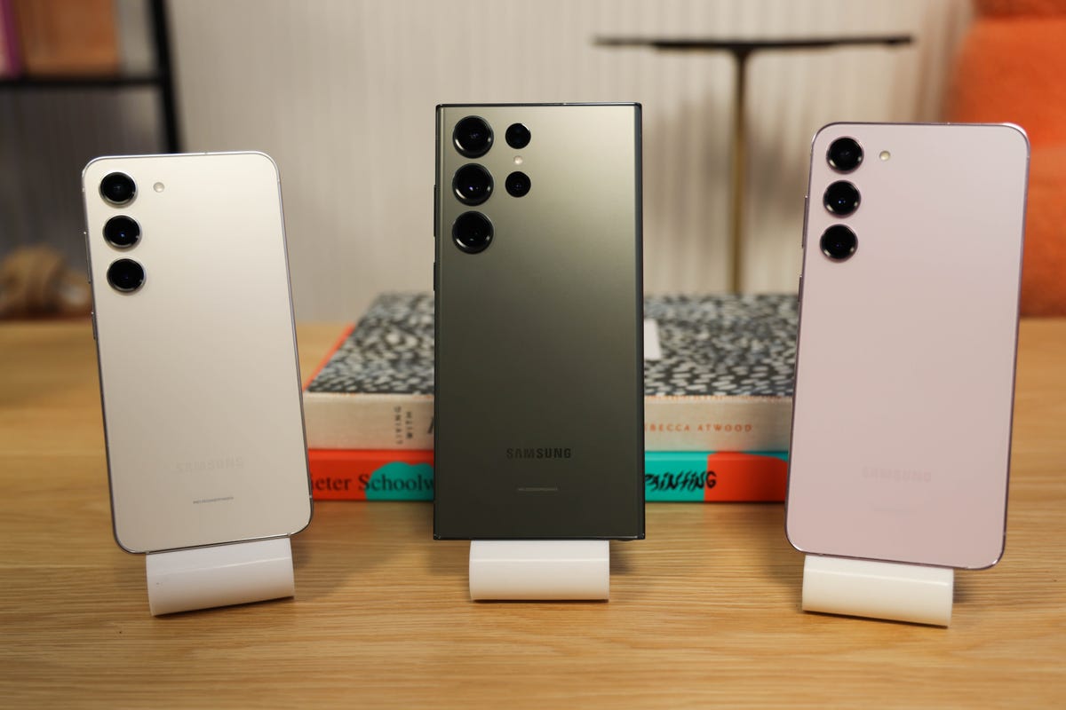 Samsung Galaxy S23, S23 Plus and S23 Ultra on stands on a wooden table, backs to us
