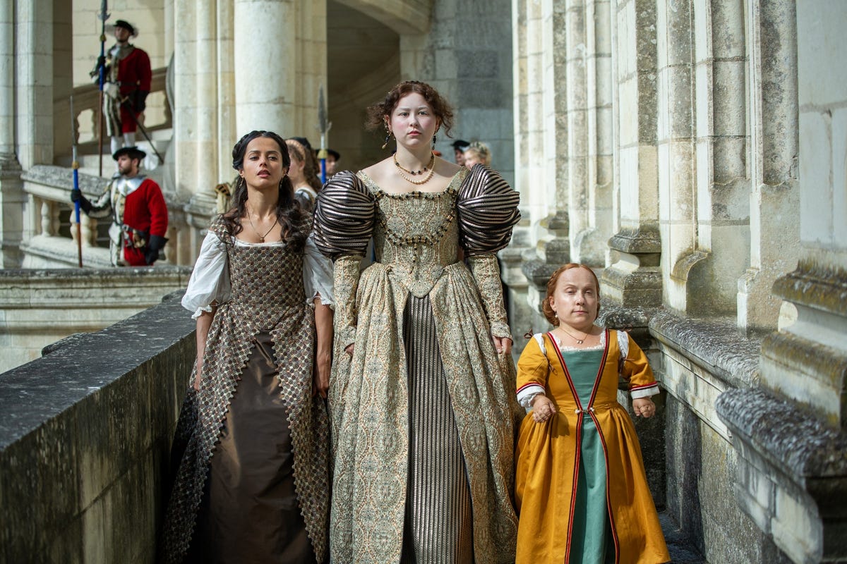 three young women dressed in medieval garb standing on castle walkway