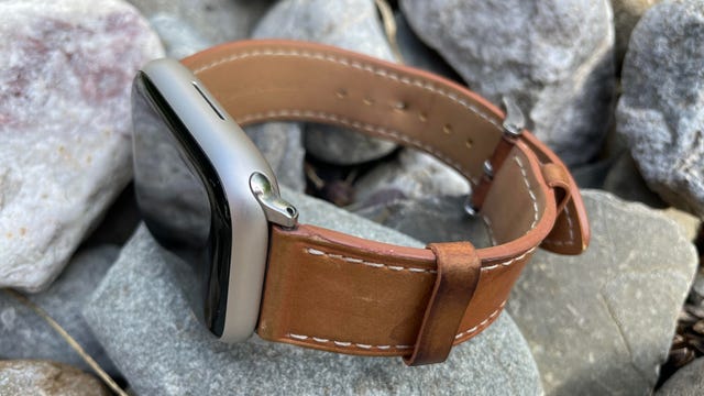 An applw watch with leather straps on pebbles