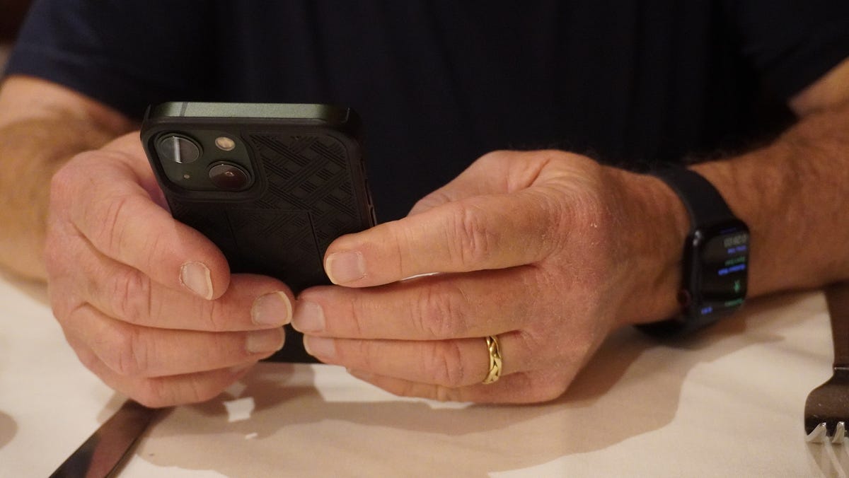 A close up of a man holding his iPhone 13 mini with an Apple Watch 8 on one wrist.