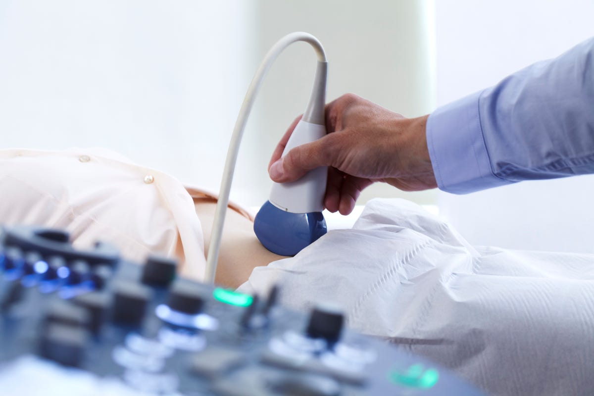 A doctor maneuvers an ultrasound instrument over a patient's stomach.