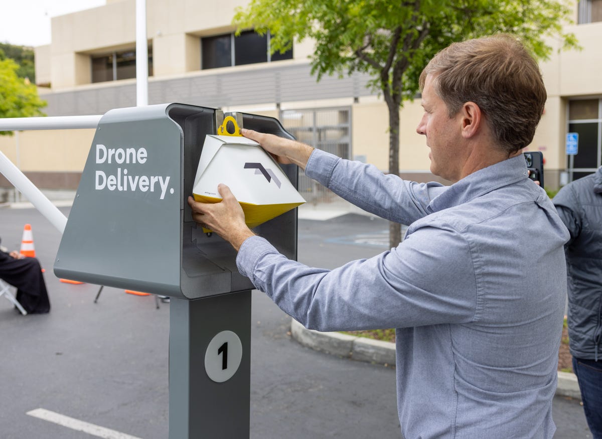 Wing marketing chief Jonathan Bass shows how a store employee hooks a package onto the autoloader to await drone pickup