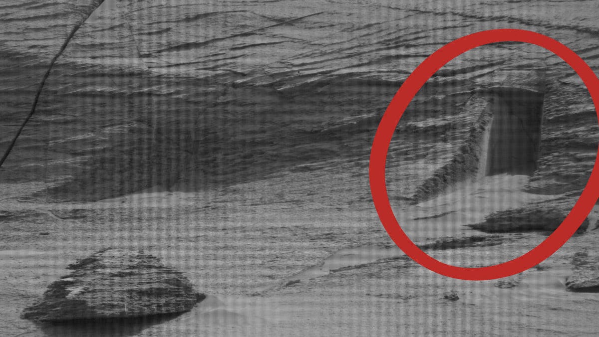 Black and white Mars image of a layered cliff with a rectangular shadowy area highlighted by a red circle.