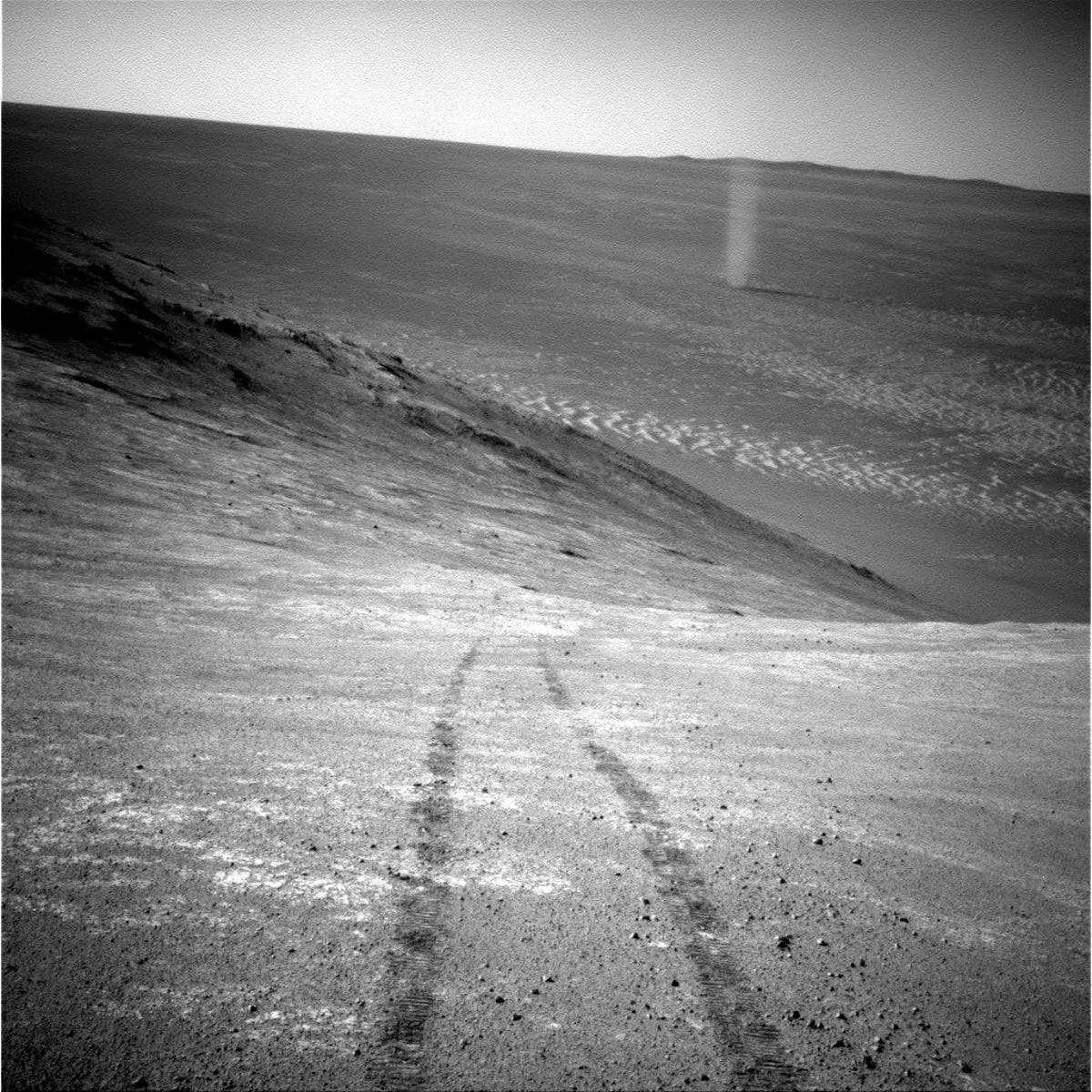 Scenic black and white landscape image with parallel rover wheels tracks and column of a dust devil in the distance.