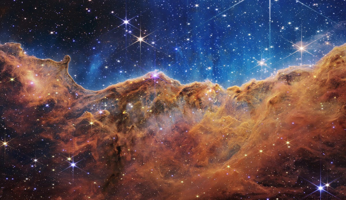 Nébuleuse de la Carène : les étoiles scintillent sur un fond indigo au-dessus des nuages ​​de gaz bronze rouillé