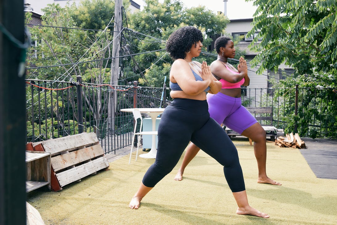 Two plus size women practice yoga on a sunny deck