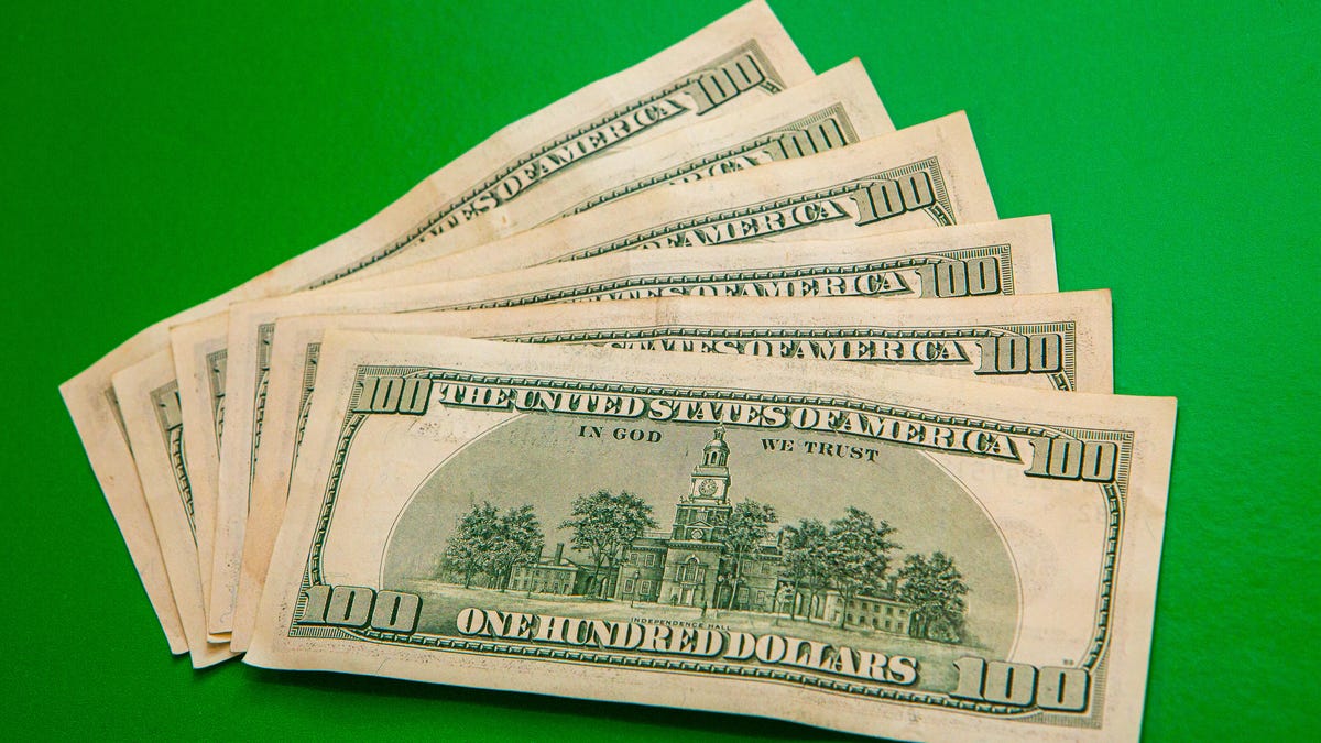 Six $100 bills fanned out against a green background