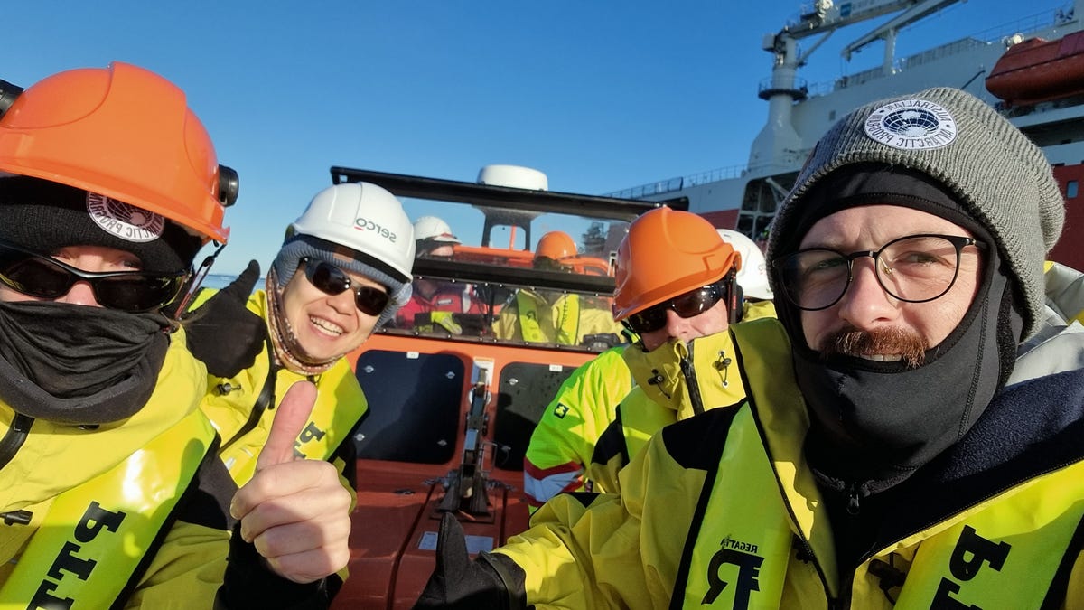 Four expeditioners pose for a photo inside a tender, wearing protective gear.
