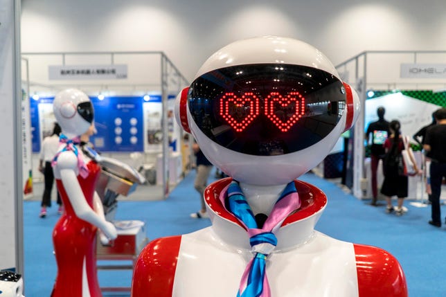 A female robot attendant at an exposition has illuminated, heart-shaped eyes.