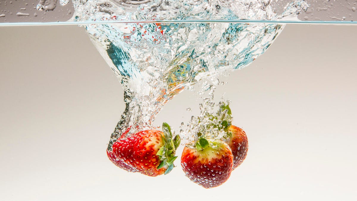Three strawberries dunking into water.