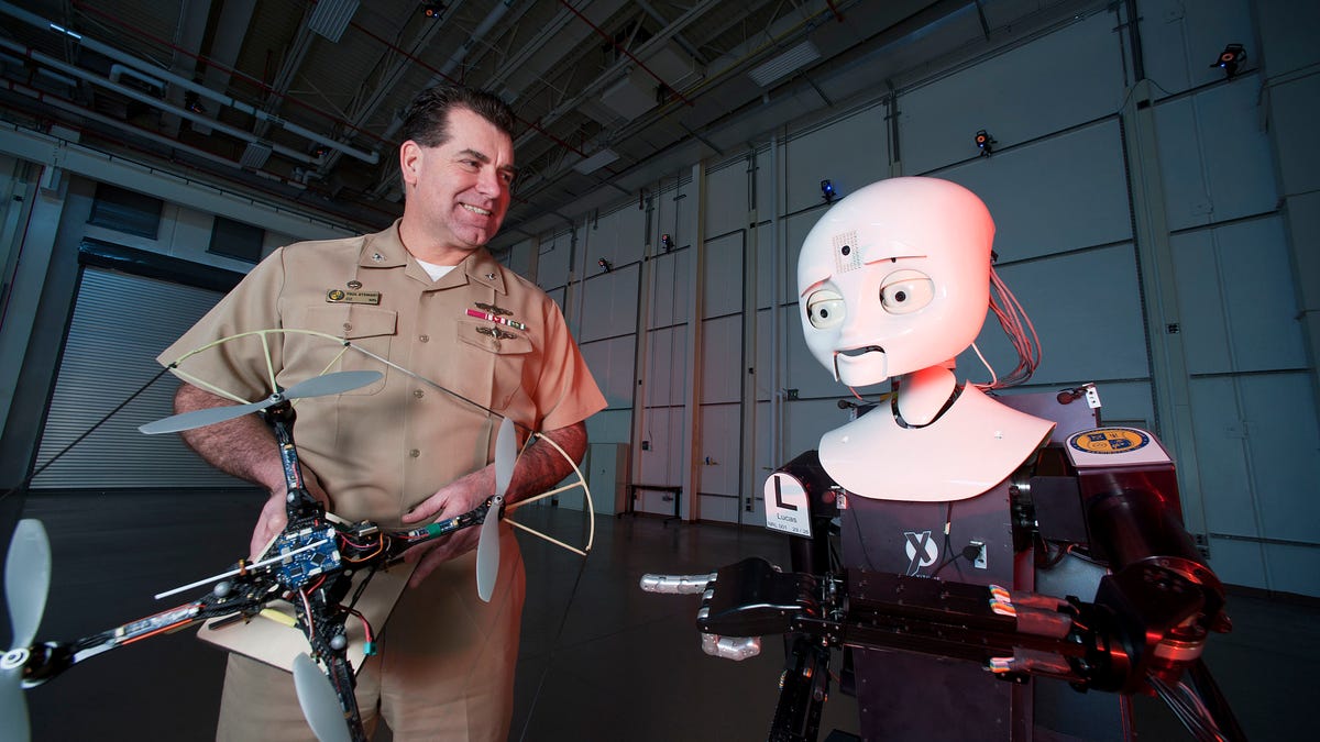 Captain Paul Stewart, the commanding officer of the Naval Research Laboratory, shows two robots from the Laboratory for Autonomous Systems Research.
