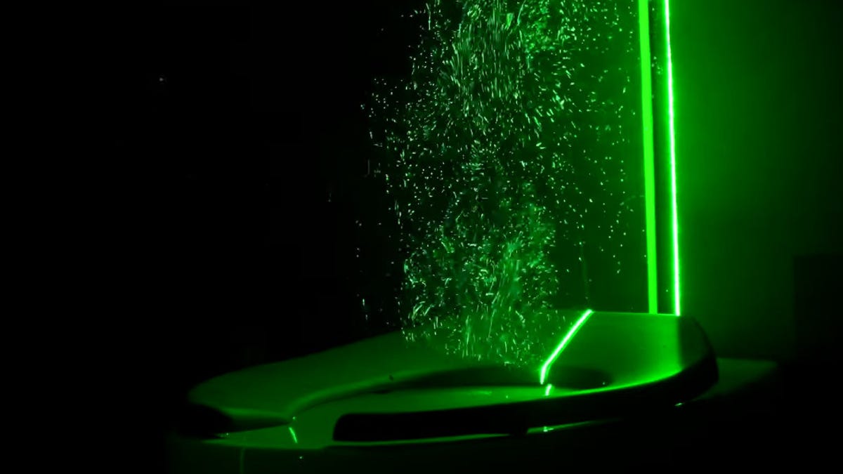 Toilet glowing in green light as droplets of water are caught shining like someone doing a spit take out of the bowl.