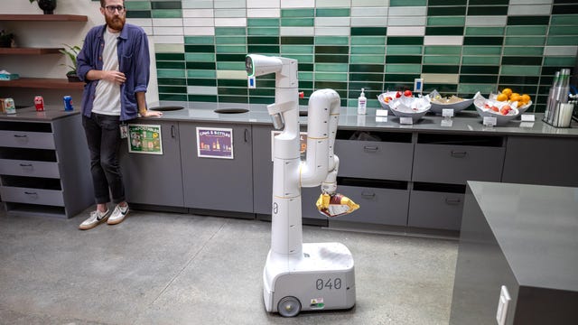 A wheeled robot carries a bag of chips through a Google office kitchen