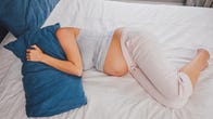Woman lying on her bed while holding a pillow over her head, tired.