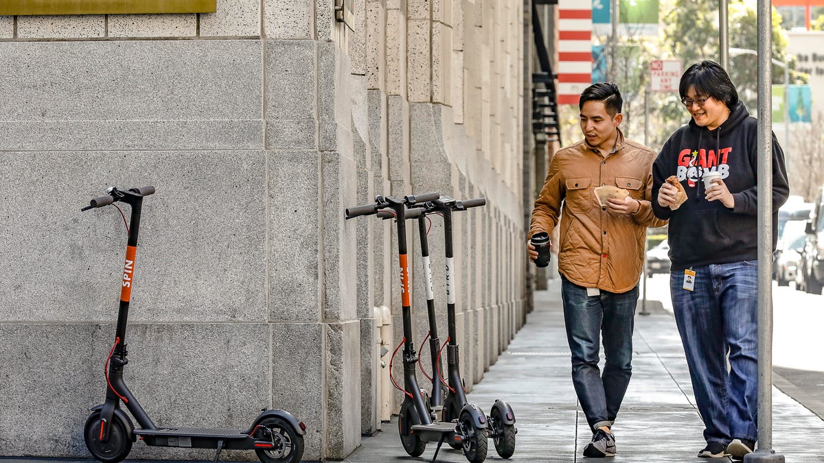 Two pedestrians taking note of a group of scooters on an SF sidewalk.