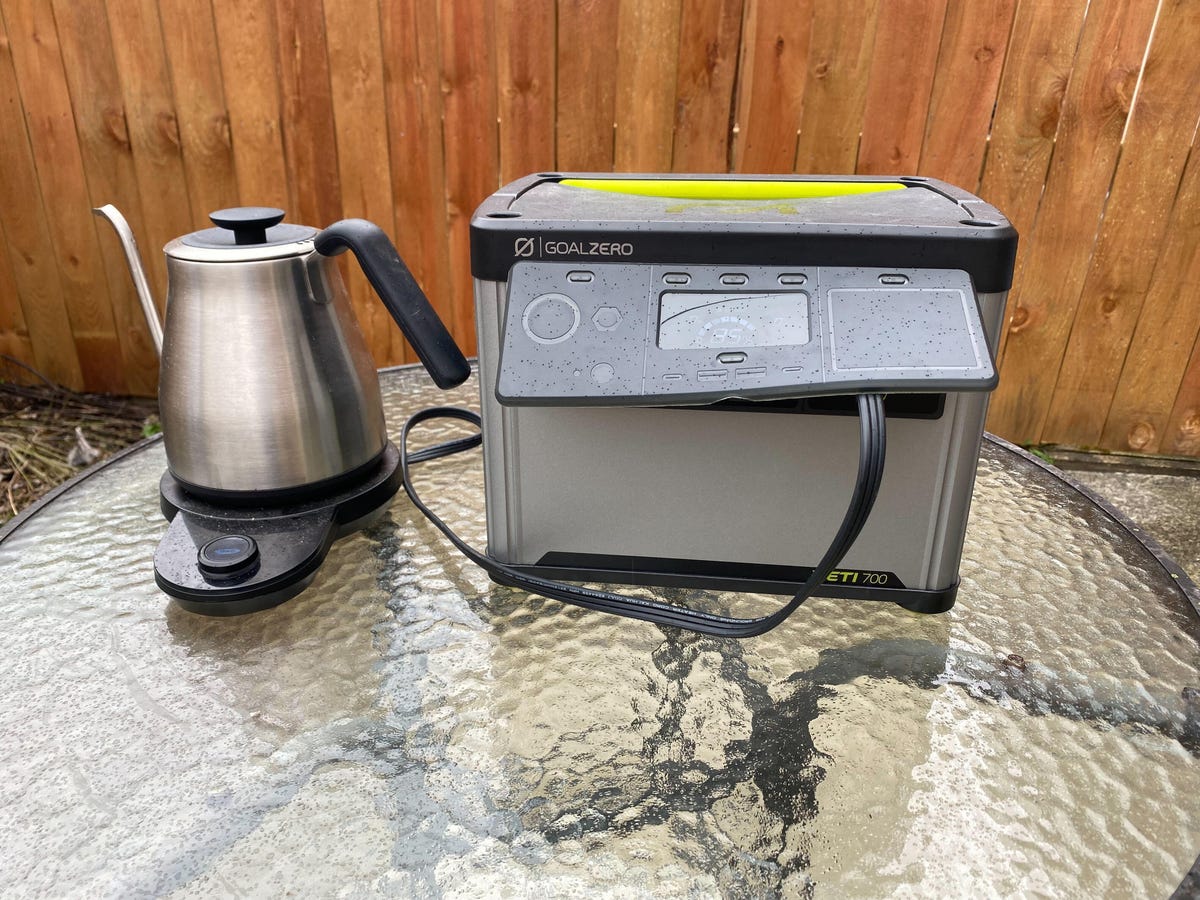 A silver and black portable power station on a glass table with a silver electric kettle next to it.