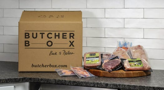A variety of meats are displayed on a counter next to a delivery box from ButcherBox.