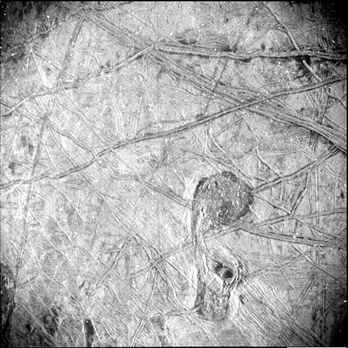 Odd-looking, striated icy crust Jupiter moon Europa with criss-crossing lines in black and white.