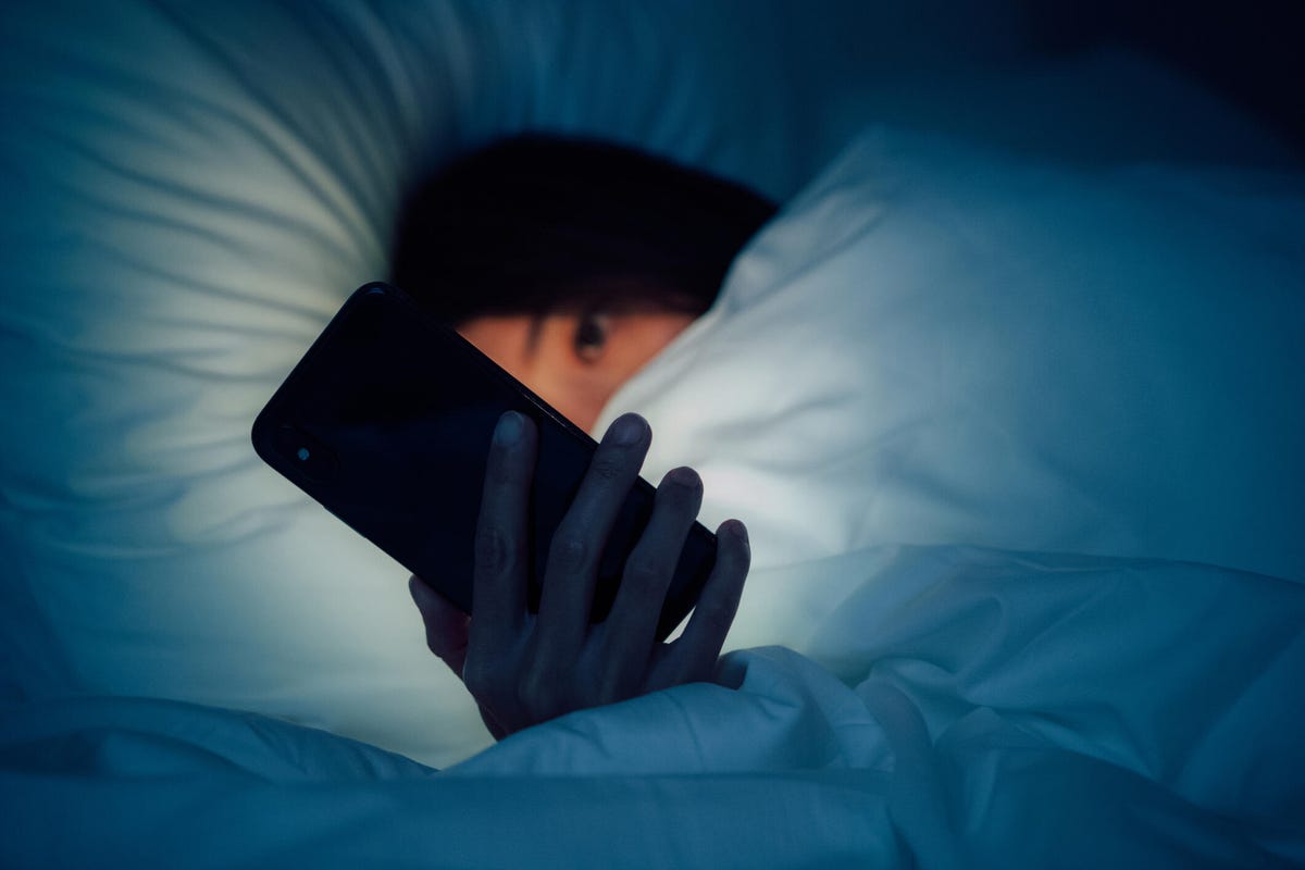 Woman holding her phone in the dark, trying to sleep