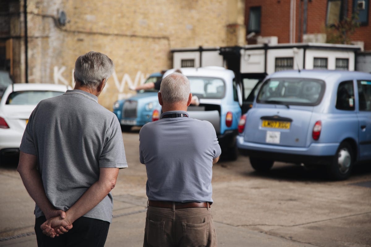 Two taxi drivers take a moment to relax and watch their cars being serviced in the Southwark cab station. The man on the right (who requested not to be named) was waiting to have his payment machines removed, having just finished his last ever trip after 48 years of driving.