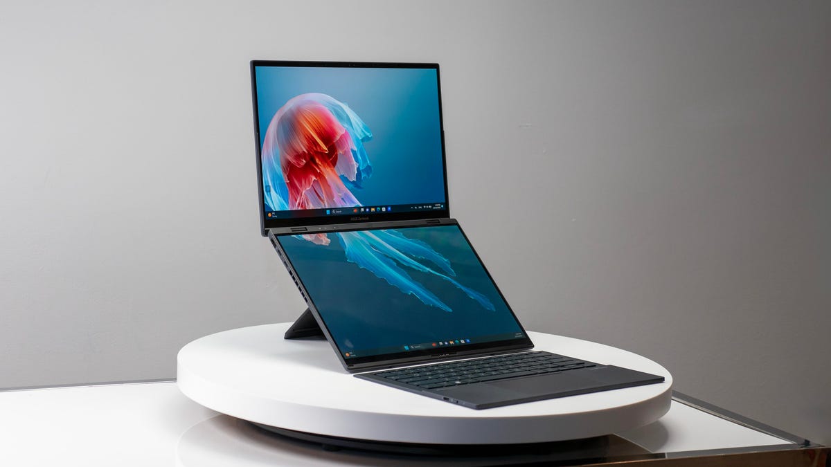 The dual-screen Asus Zenbook Duo open and facing to the right, resting on its rear kickstand with its removable keyboard sitting on a desk in front of the bottom display.