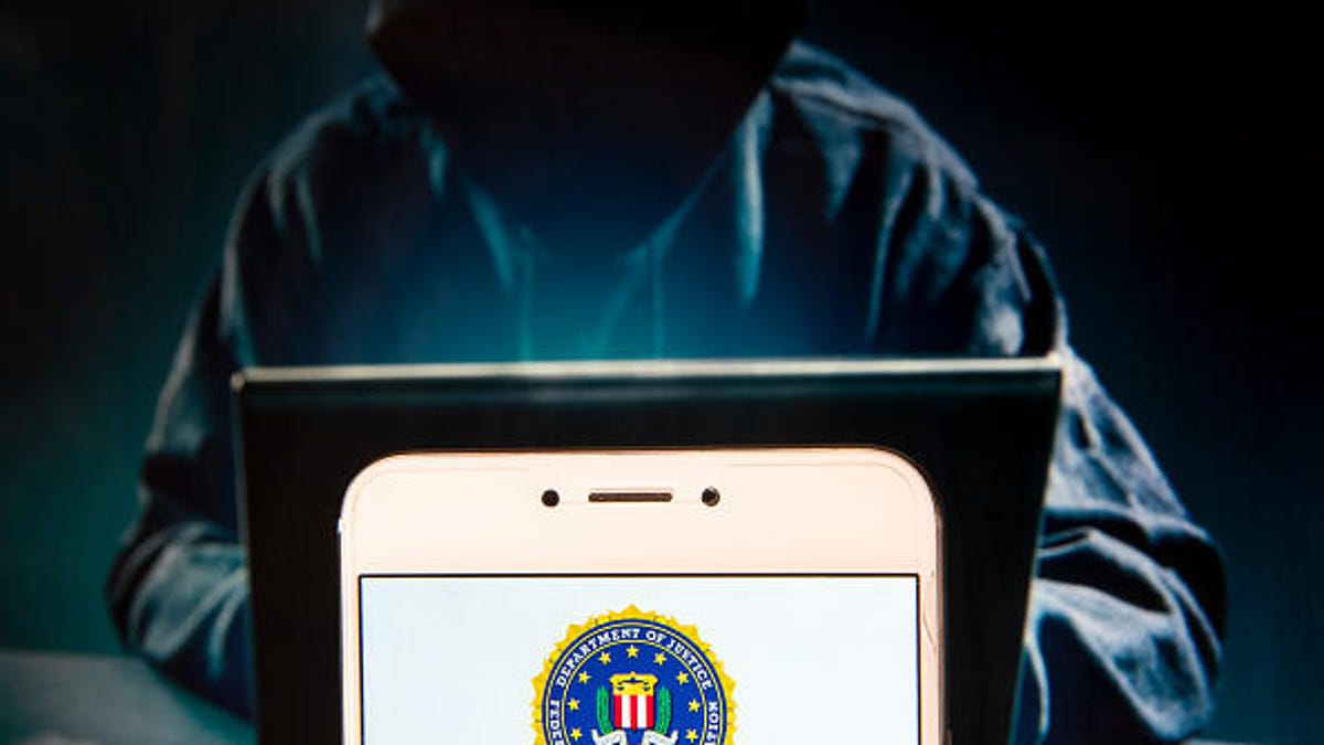 FBI logo on a phone screen in front of a dark image of a hooded figure at a computer