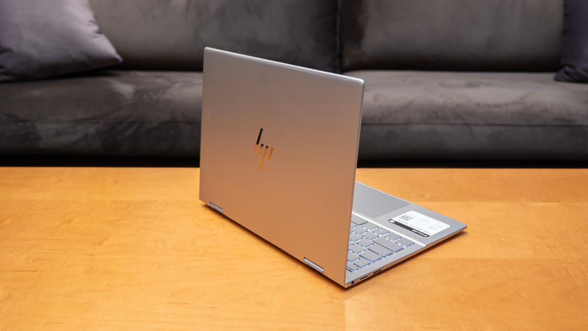 A silver 13-inch HP Envy x360 13 two-in-one laptop sitting on a wood table.
