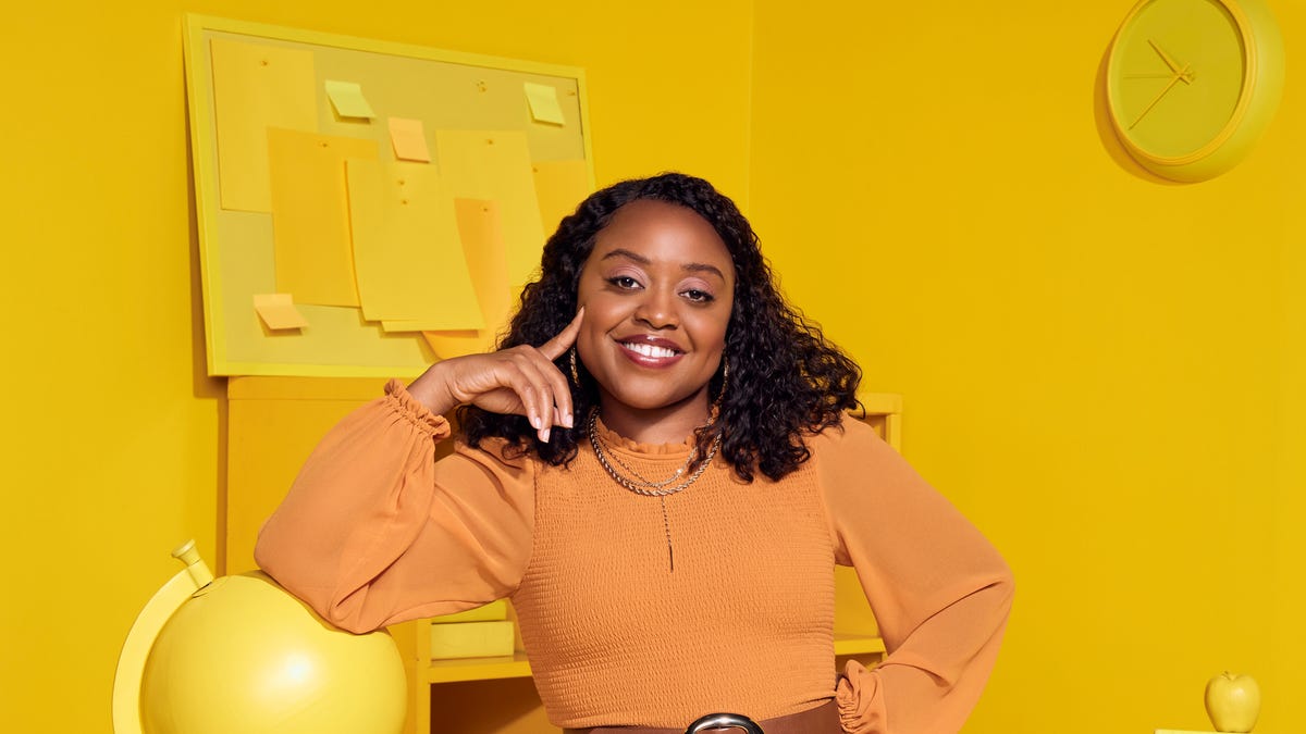 Actor Quinta Brunson smiles in front of a yellow-painted blackboard.