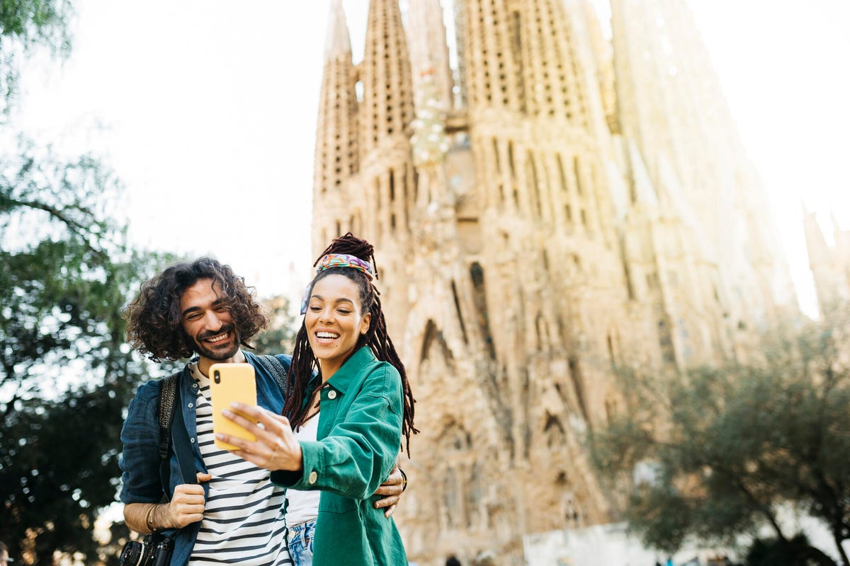 A man and woman stand posed to take a selfie in front of a cathedral in Spain.
