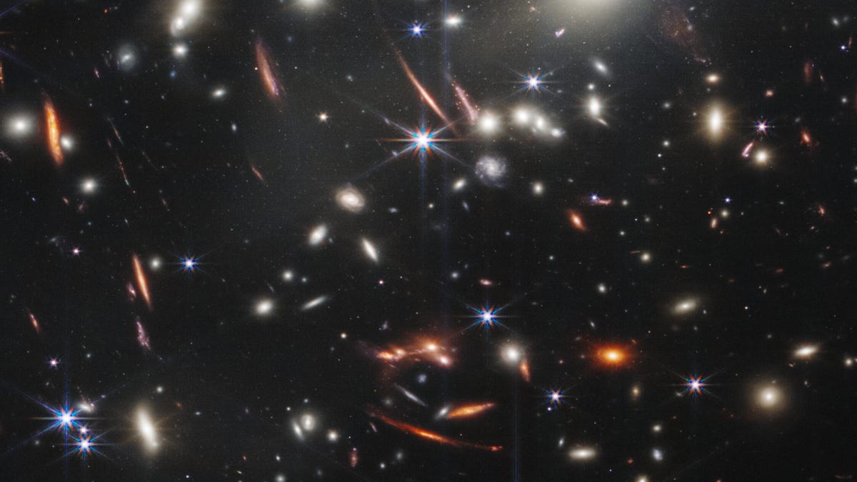 An image of deep space showing hundreds of galaxies against the black void. Galaxies are red, yellow, white and blue