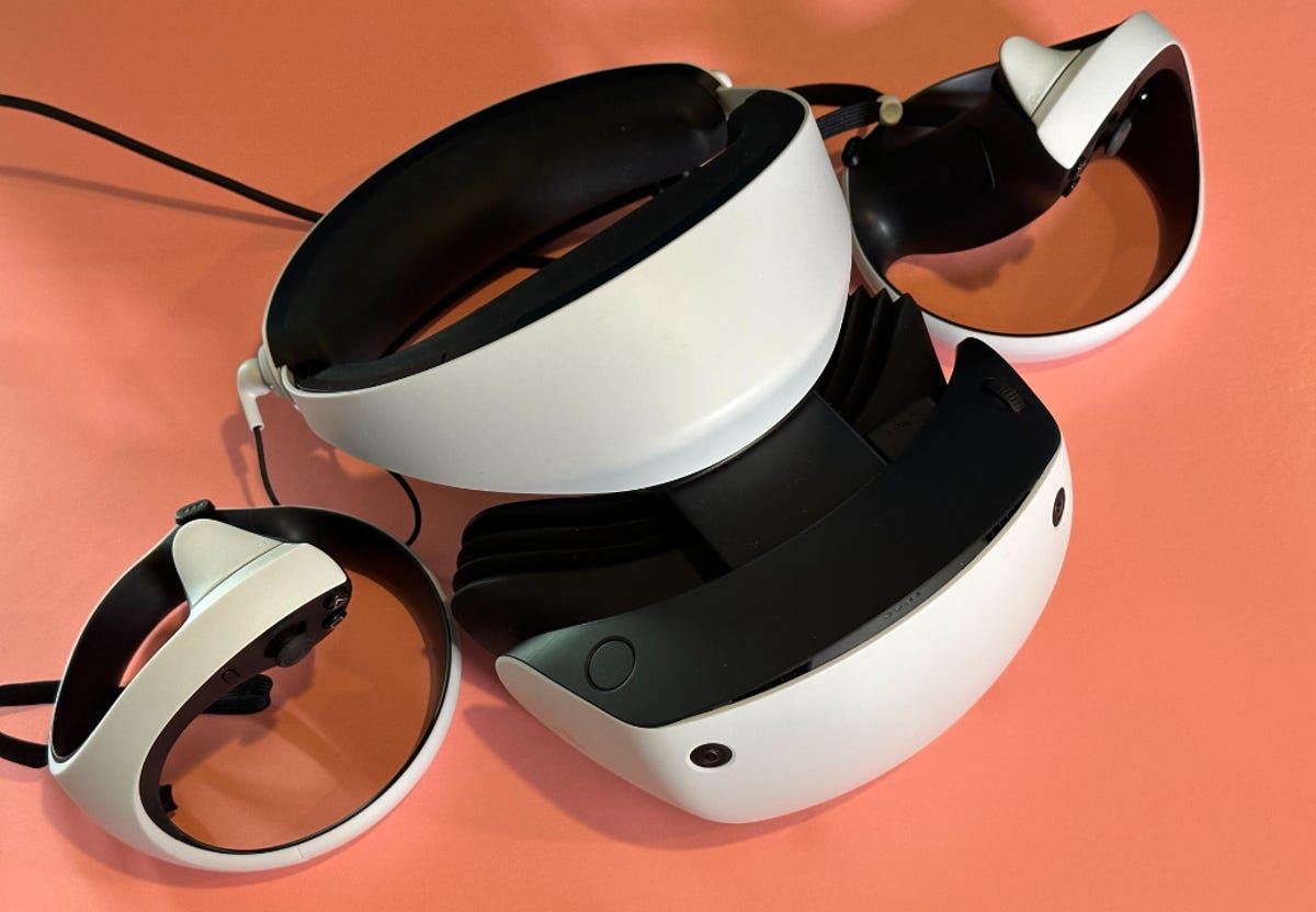 PlayStation VR 2 headset and hand holds in white against a peach background